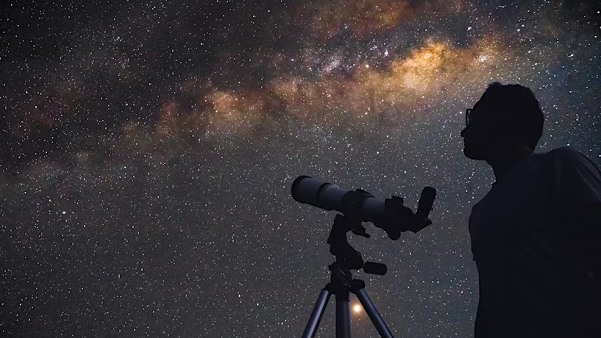 Photo of a person with a telescope looking at the night sky
