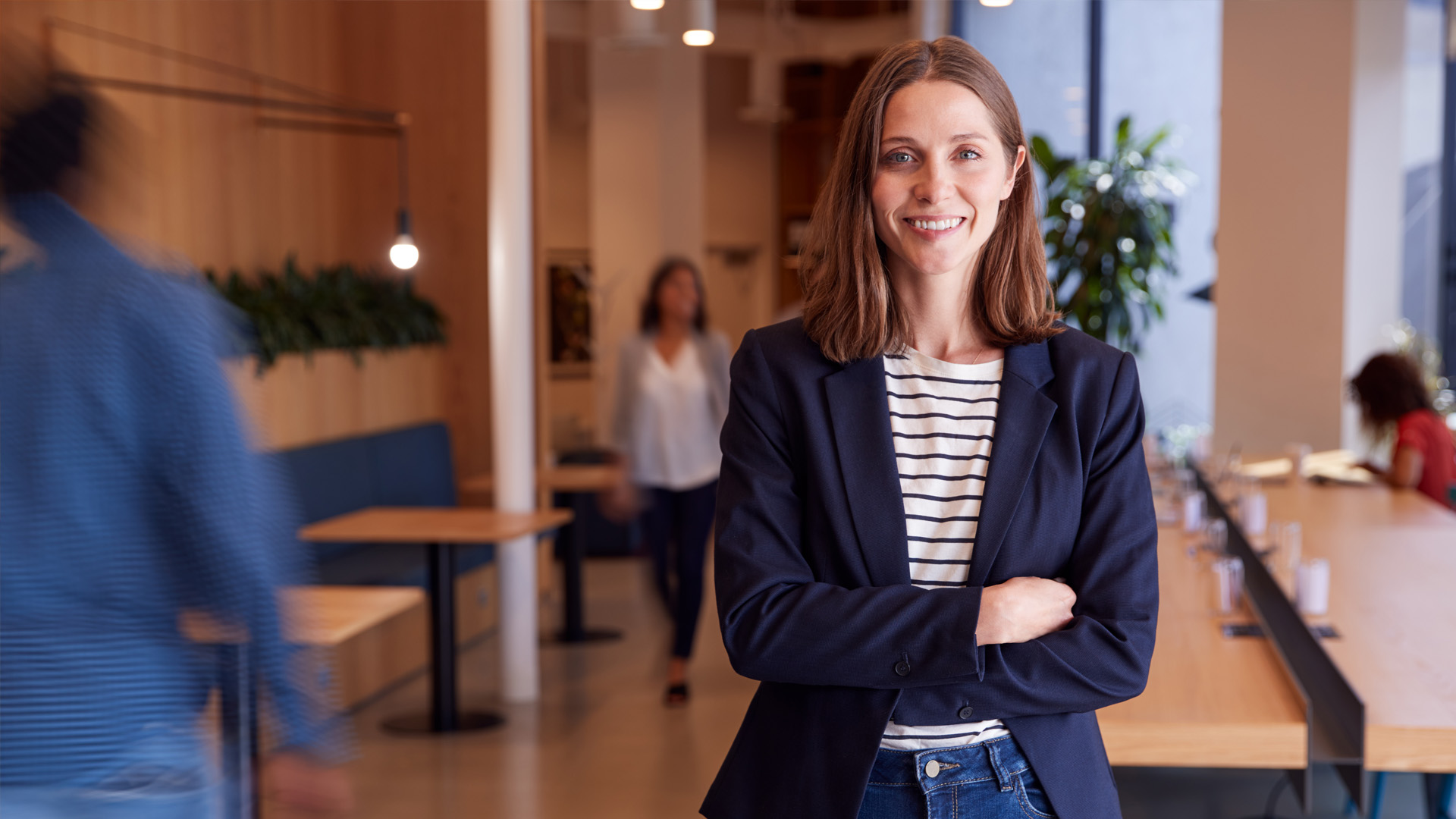 Portrait Of Businesswoman Standing In Busy Modern Open Plan Office With Colleagues In Background