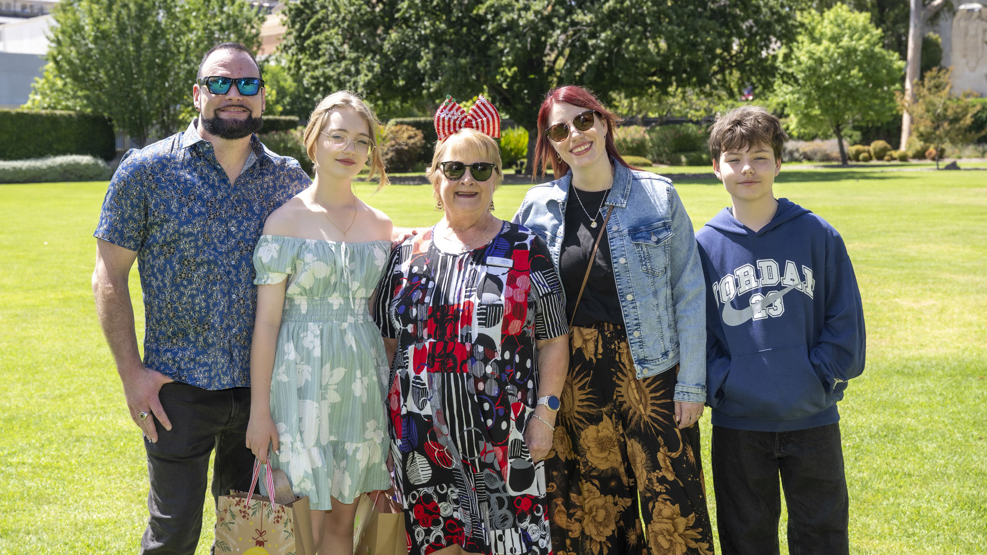 Five family members posing outside, standing close together and smiling at the camera.