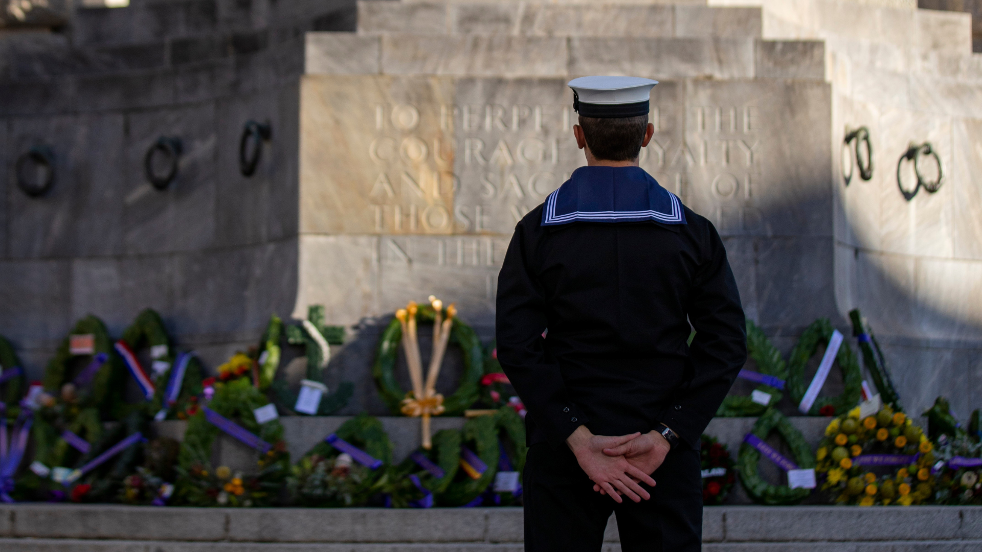Australian Navy personnel standing before a war memorial during a commemorative service.